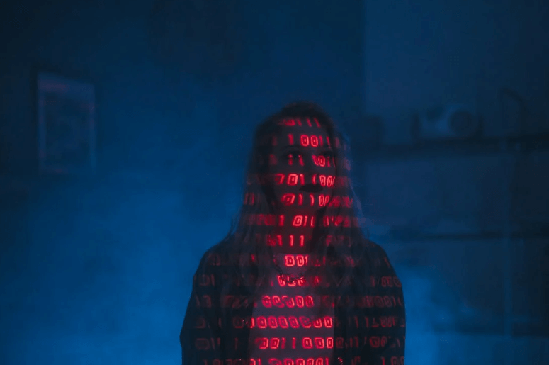 Sötét háttérben álló alak digitális kódokkal megvilágítva